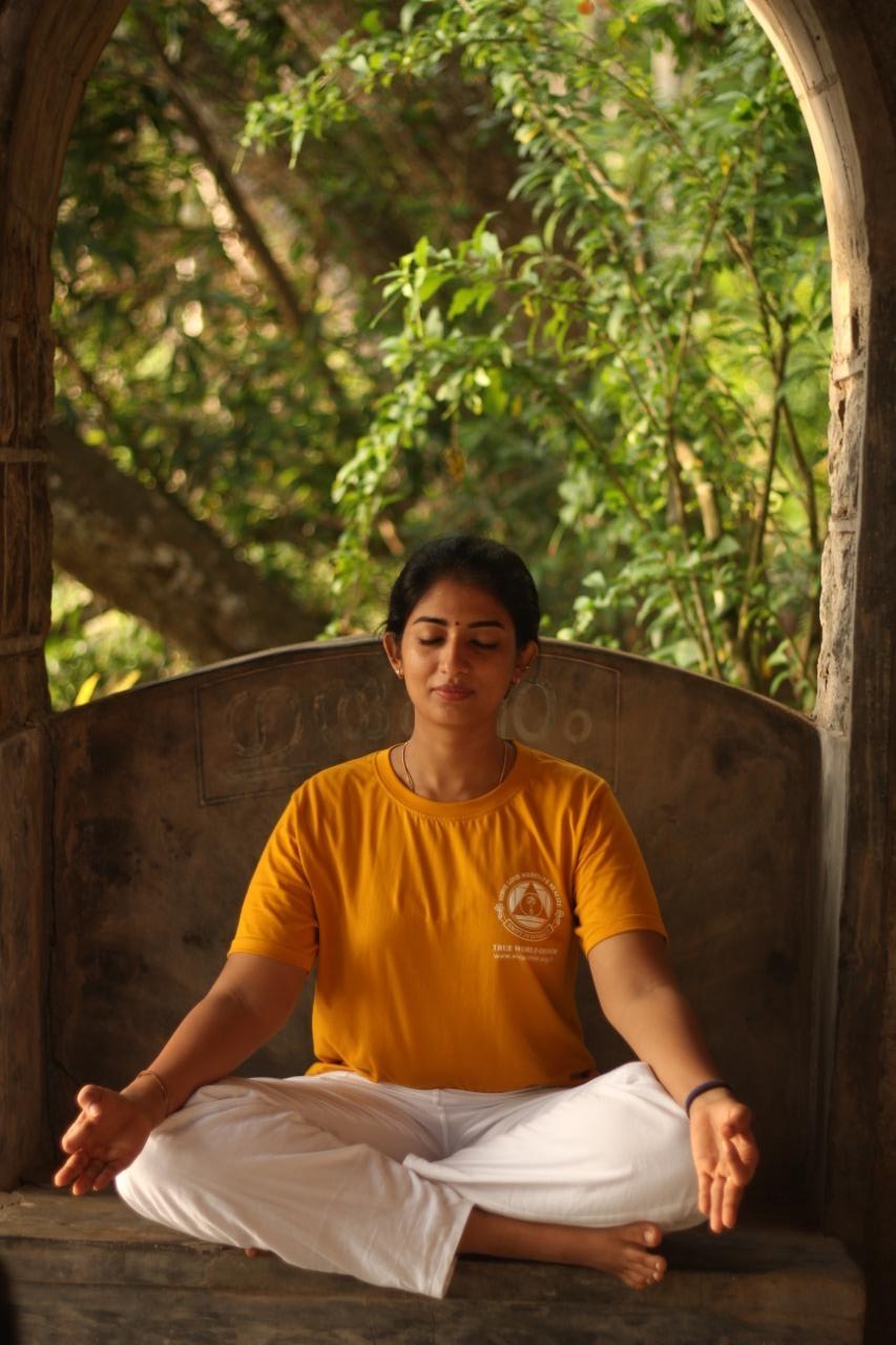 Sreepriya practising a seated mudra amid greenery